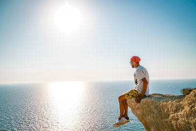 Man sitting on rock over sea against sky