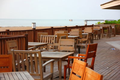 Empty chairs and tables at beach against sky