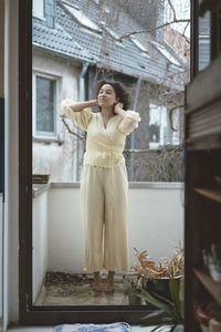 Woman with hands behind head standing on balcony at home