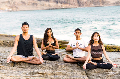 Friends doing yoga on rock at beach