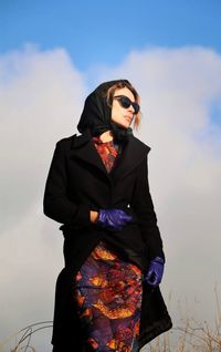 Young woman wearing sunglasses standing against sky