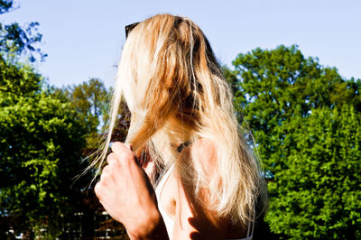 Side view of young woman standing against trees at park