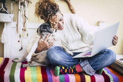 Woman embracing dog while using laptop on bed at home