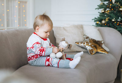 Cute little baby girl in winter overall in the room with christmas tree at the home, happy new year