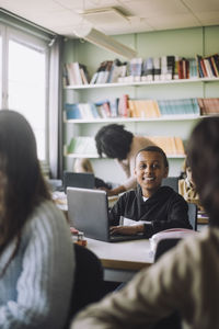 Smiling student with laptop sitting at desk in classroom