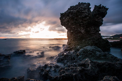 Rock formation on beach against sky during sunset