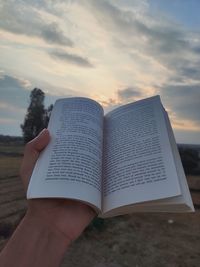 Midsection of person holding book against sky