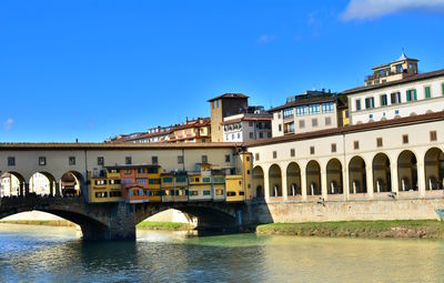 Arch bridge over river in city against blue sky