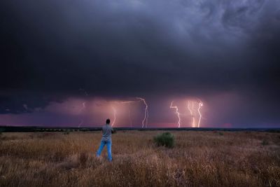 Rear view of man standing on field against storm clouds