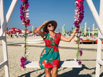 Portrait of woman wearing hat sitting on swing at beach