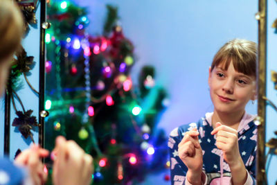 Llittle blonde caucasian girl 10 years old in pajamas shows korean gesture heart on mirror