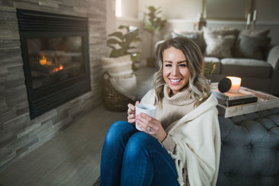 Portrait of smiling young woman holding coffee while sitting at home