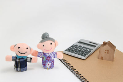 Close-up of figurines by spiral notebook and calculator against white background