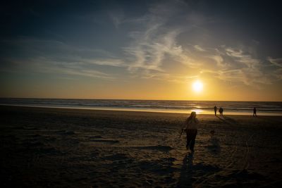 Silhouette people on beach against sky during sunset