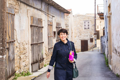 Portrait of smiling young woman standing on alley amidst buildings in city