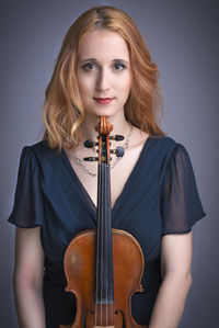 Close-up portrait of young woman with violin against gray background