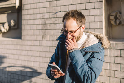 Adult male with glasses looking into smartphone and laughing. concept of pleasant emotions.