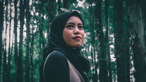 Young woman standing against trees in forest