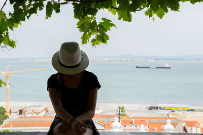 Woman smoking cigarette while sitting on retaining wall against sea