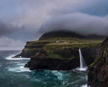 Scenic view of cliff by sea against cloudy sky