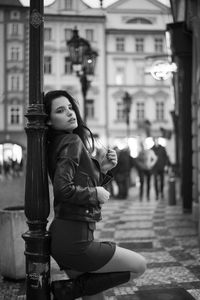 Seductive woman leaning on street light at sidewalk in city