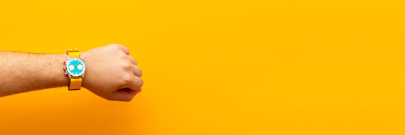 Cropped hand of woman holding thermometer against yellow background