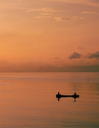Silhouette people riding on sea against orange sky