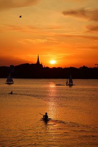 Silhouette people on sea against orange sky