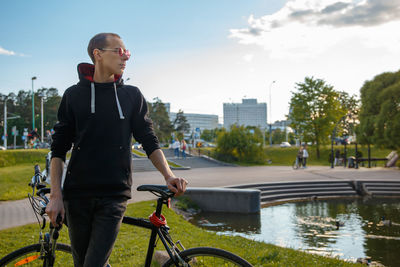 Young man with bicycle in city against sky