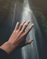Close-up of hand against waterfall