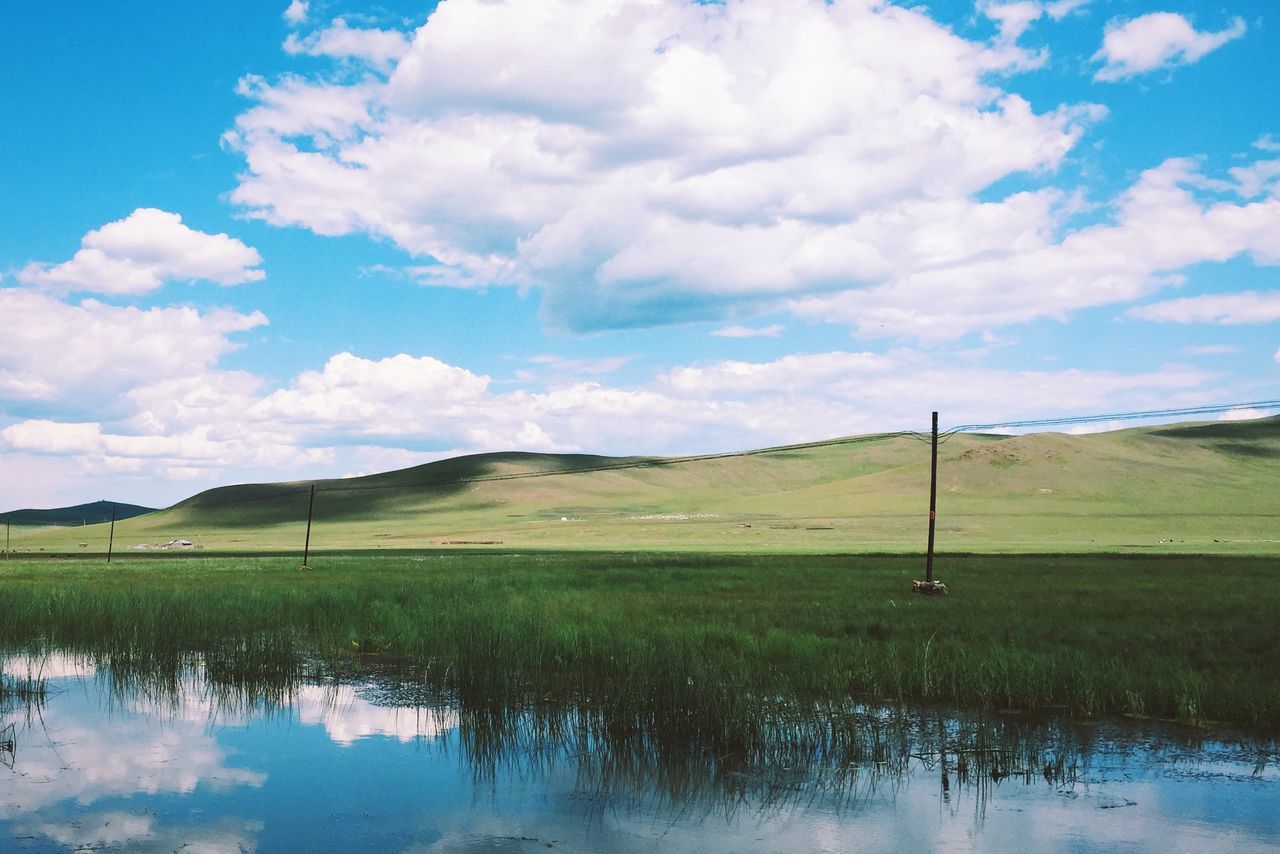 sky, tranquil scene, tranquility, grass, water, scenics, landscape, lake, beauty in nature, field, cloud - sky, blue, cloud, nature, reflection, grassy, countryside, rural scene, idyllic, non-urban scene