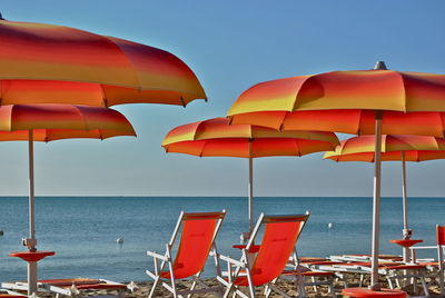 Orange deck chairs with parasols at beach against clear sky