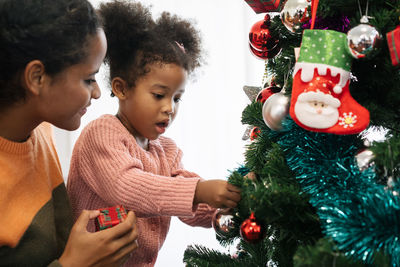 Mother and daughter holding decoration on christmas tree