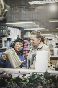 Saleswoman showing kettle to smiling female customer in store seen through glass window