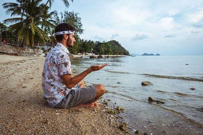 Man sitting at beach against sky