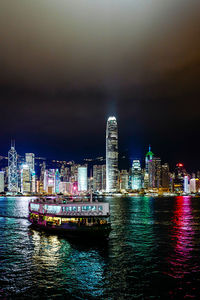 Ferry boat on river with illuminated skyline against sky