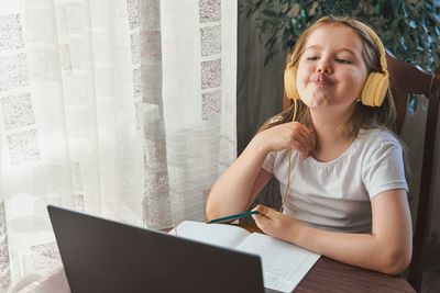 Little girl uses a laptop and shows her teeth and smile to study at home with a speech therapist. 