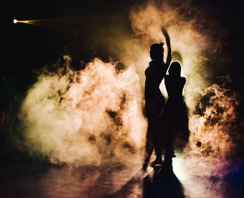 Silhouette of a woman dancing between lights and smoke unrecognozible person