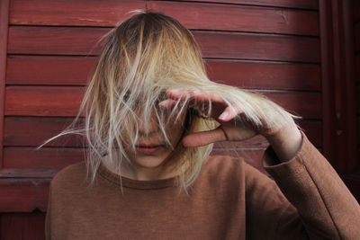 Portrait of young woman with tousled hair standing against wooden wall