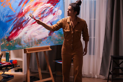 Beautiful female painter holding paintbrush while painting at workshop