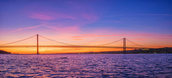 Suspension bridge over river against sky during sunset