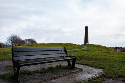 Empty bench on field against sky