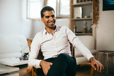 Smiling young man sitting on chair at home