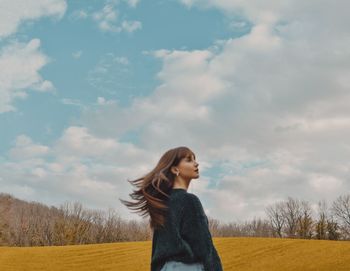 Young woman looking away while standing on field against sky