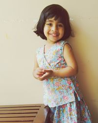 Portrait of cute smiling girl standing against wall at home