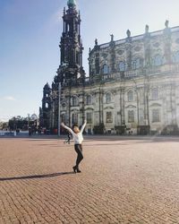 Woman with arms raised standing against built structure in city