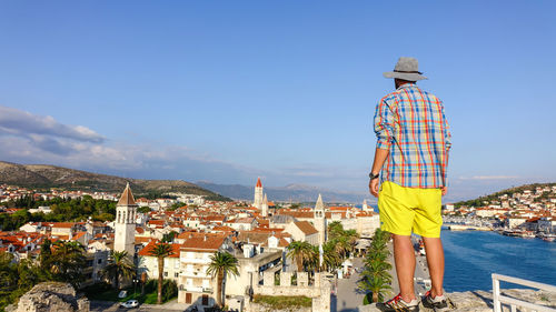 Rear view of man looking at cityscape against sky