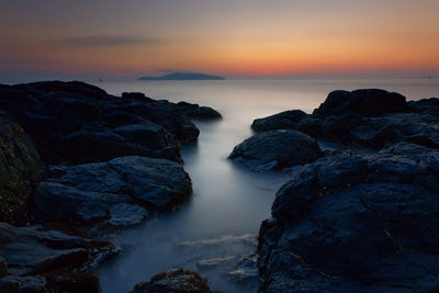 Rocks in sea against sky during sunset