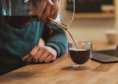 Midsection of man pouring coffee in glass on table