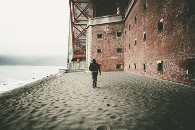 Rear view of man walking by sea against sky